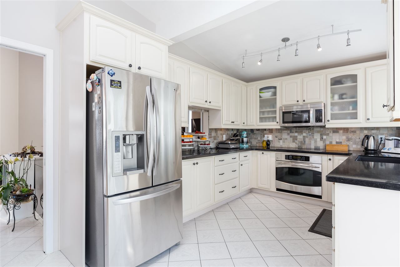 The kitchen, white cabinets around dark counters with the stainless fridge beside the door.