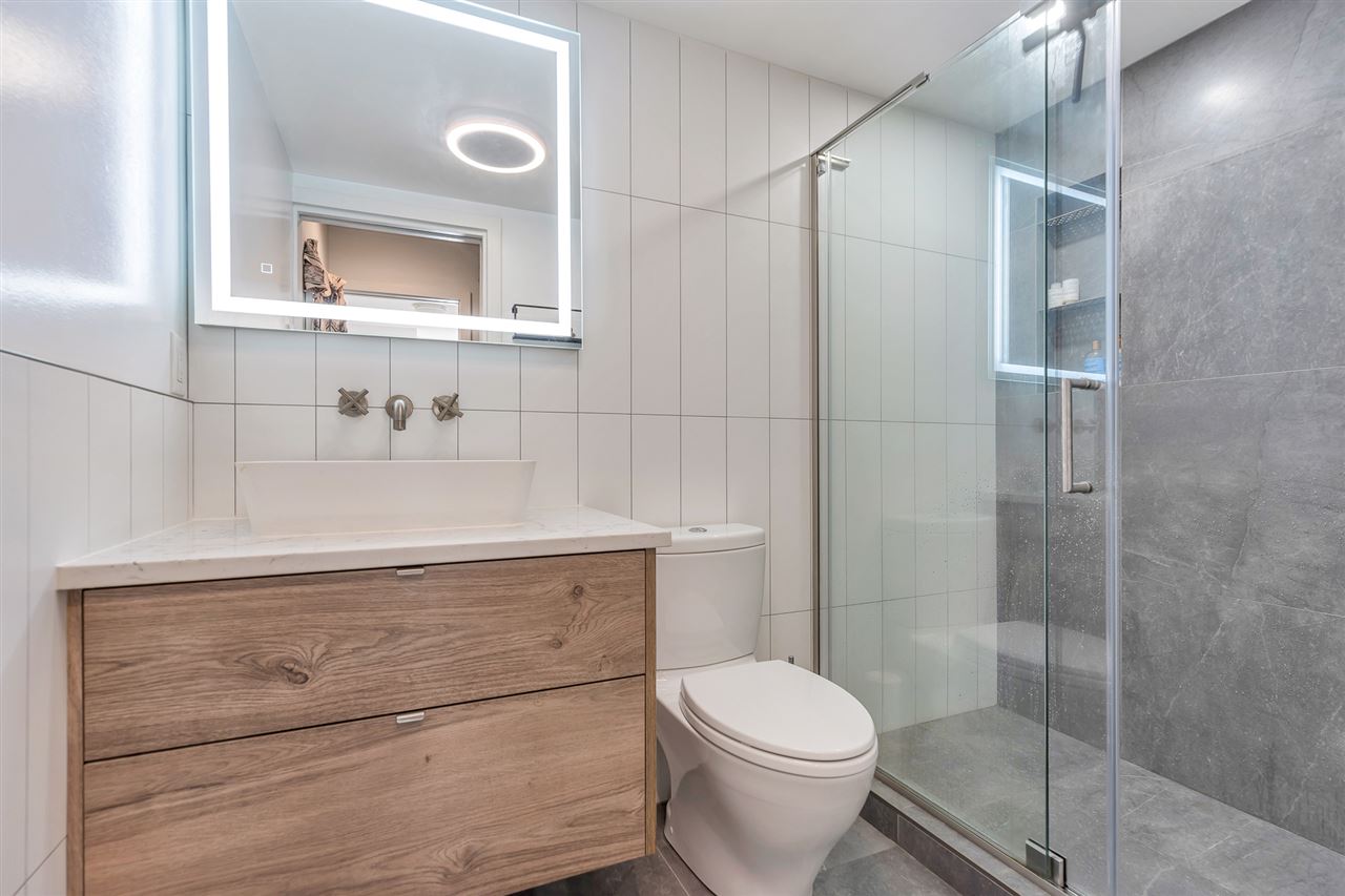 The rebuilt primary bathroom, a glass shower beside a lit mirror and a timber vanity.