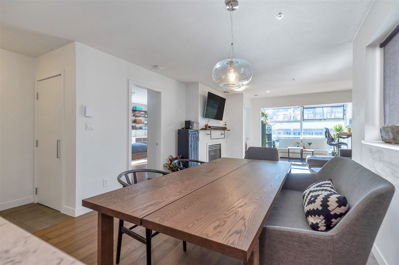 The dining table under a glass pendant, the living room and the fireplace behind it.