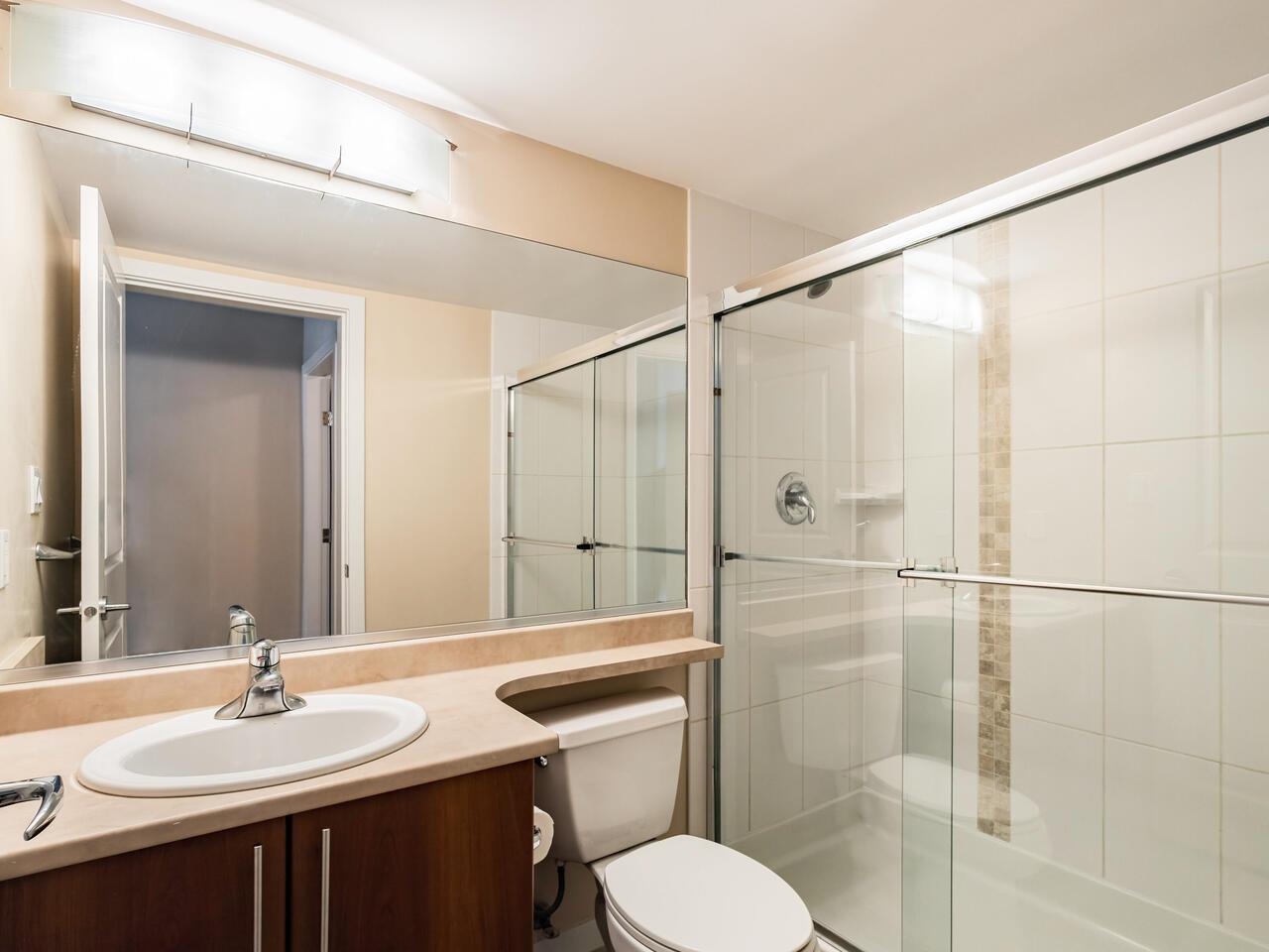 The ensuite, a long vanity under a full-width mirror with the shower glazed beside it.