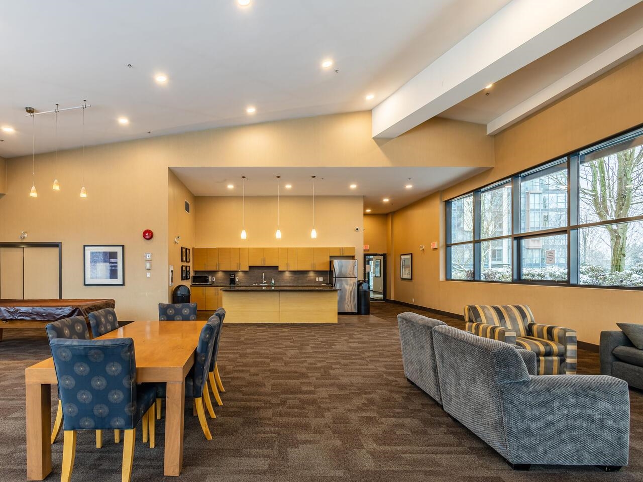 The clubhouse lounge, a long table and armchairs beside a kitchen at the far end.