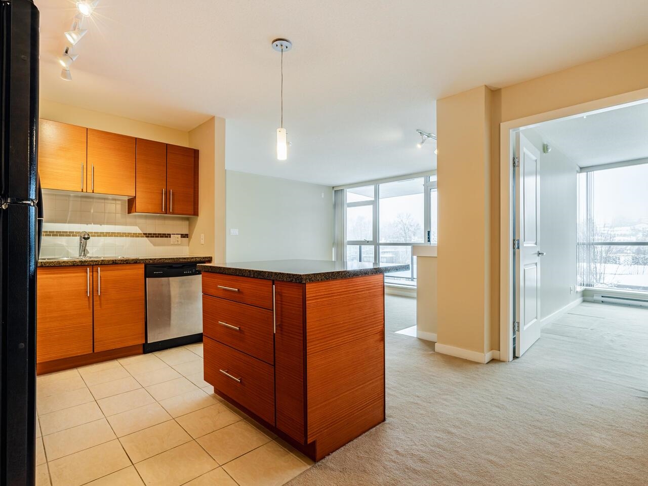 The kitchen island in warm timber under a granite top, the living room windows past it.