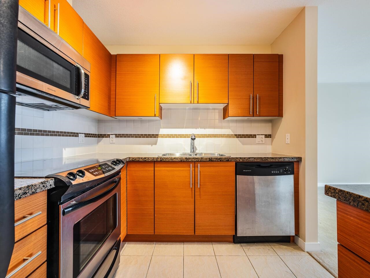 The kitchen work wall, a range and dishwasher in stainless beside the sink under a tiled splashback.