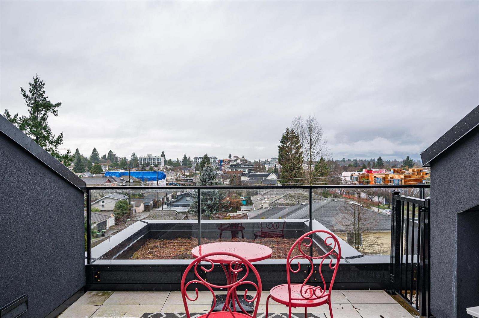 The private roof deck, a table and chairs behind a glass balustrade with the rooftops and trees beyond.