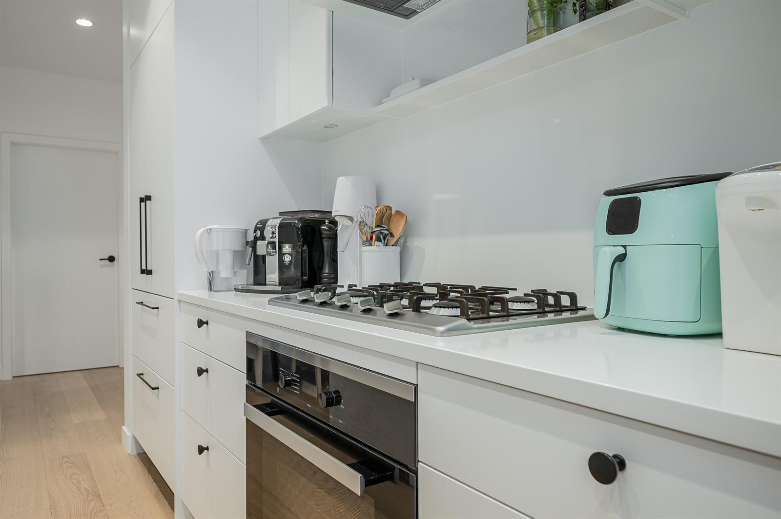 The cooking run, a gas cooktop and built-in oven set into white counters along the wall.