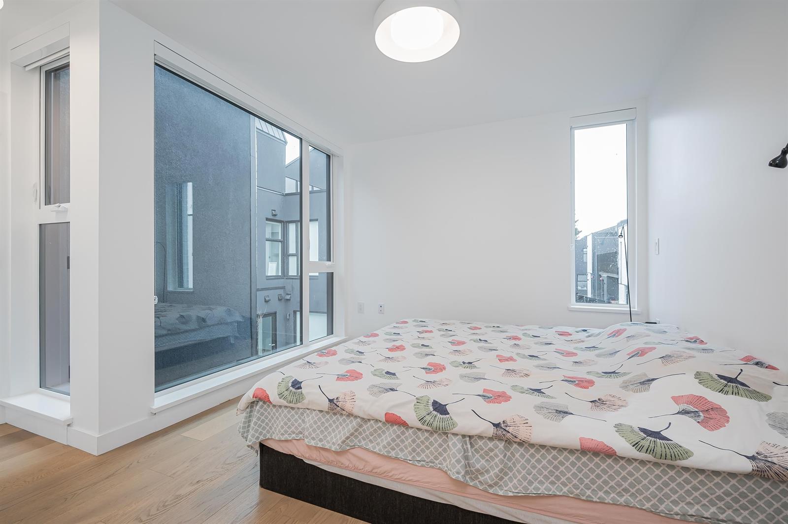 A bedroom with a wall of glass looking across the mews to the houses opposite, and a tall window on the far wall.