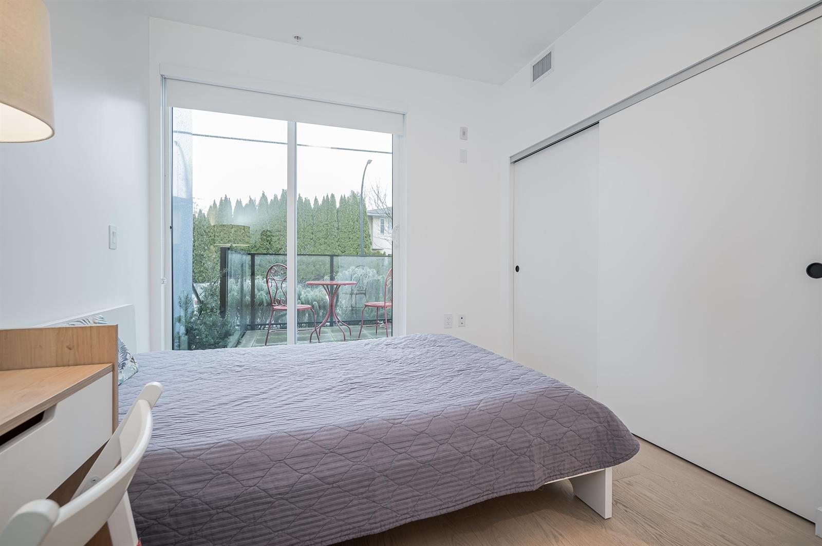 A bedroom with a sliding door out to a deck and trees beyond it.