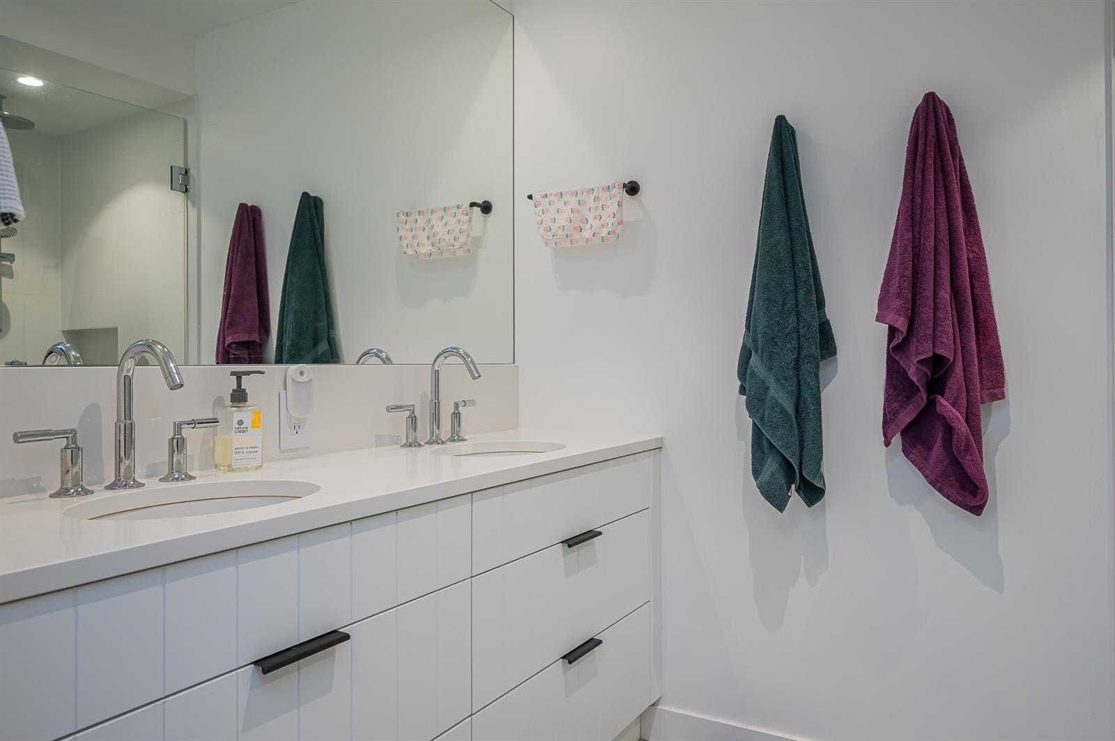 The bathroom, twin basins along a white counter beneath a full-width mirror.