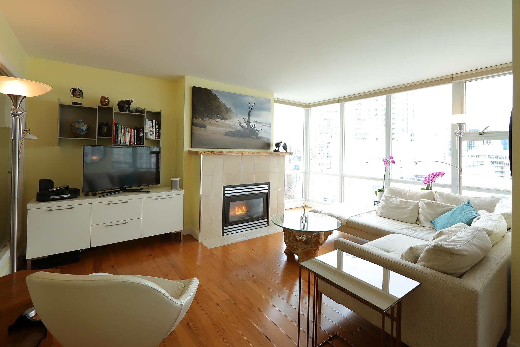 The living room, a lit gas fireplace tiled to the floor under a live-edge mantel, with the windows turning the corner beside it.