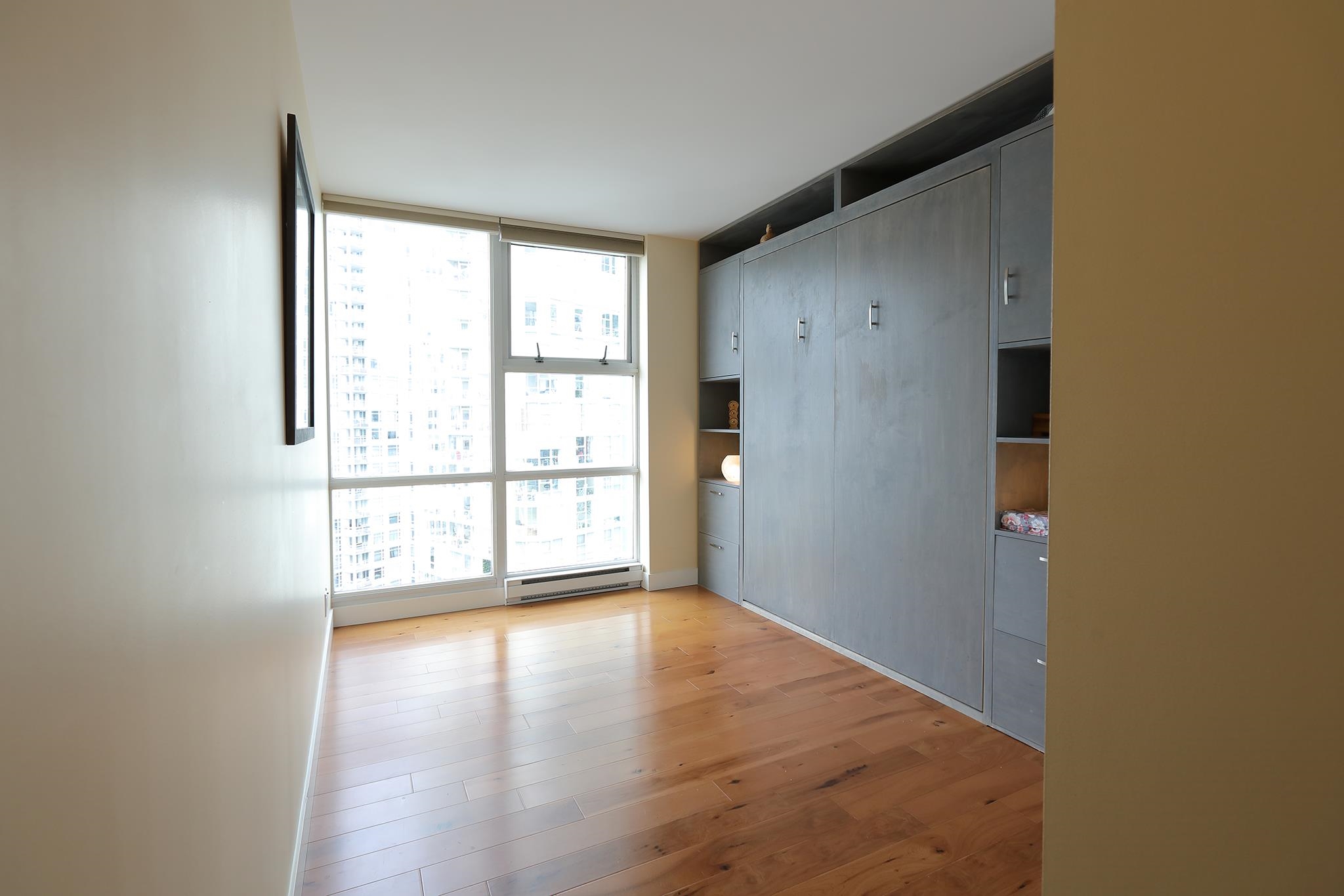 A bedroom, empty, with a wall of built-in cabinetry and windows across the corner.