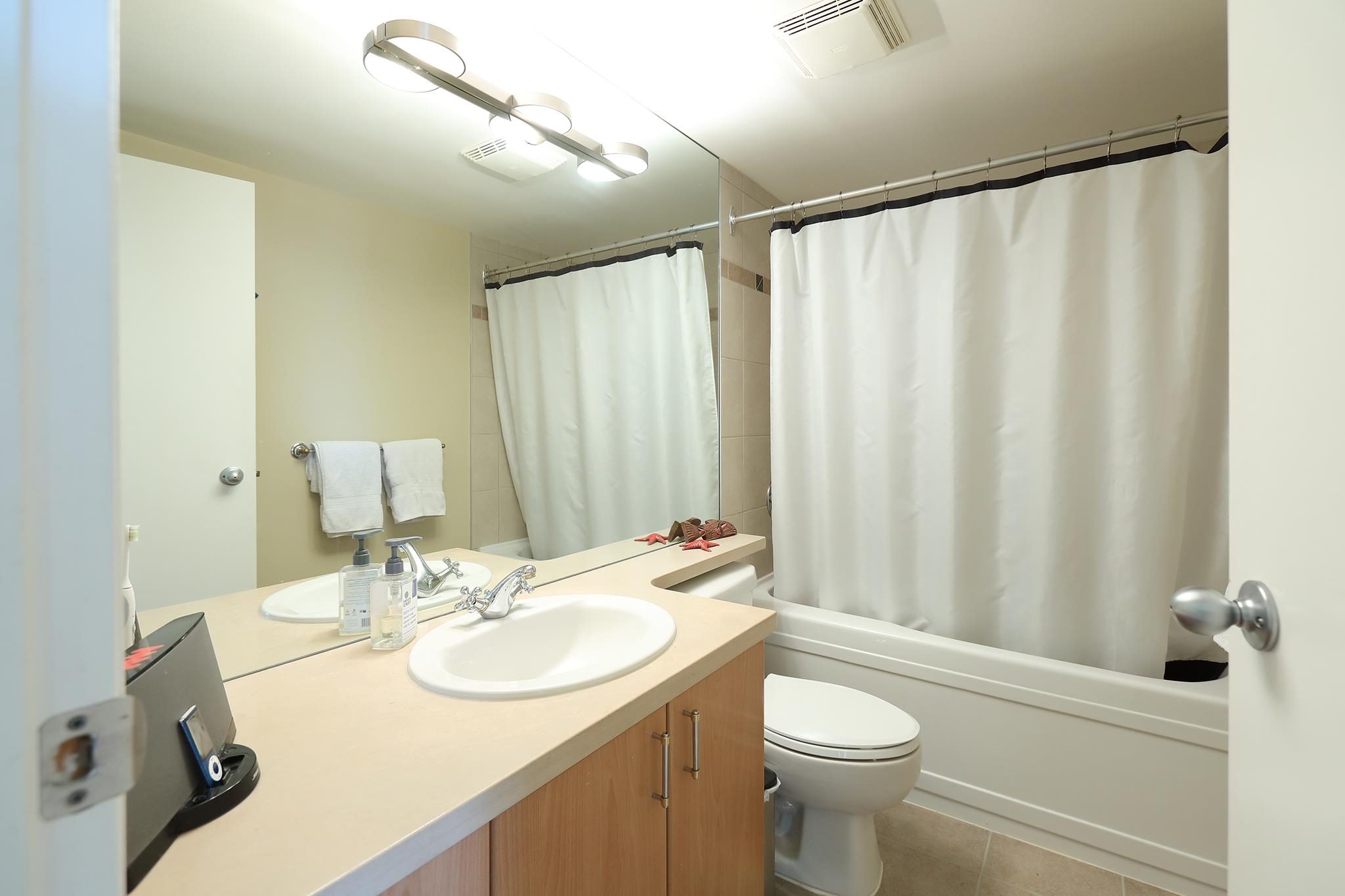 The second bathroom, a long vanity under a full-width mirror with the tub behind the curtain.