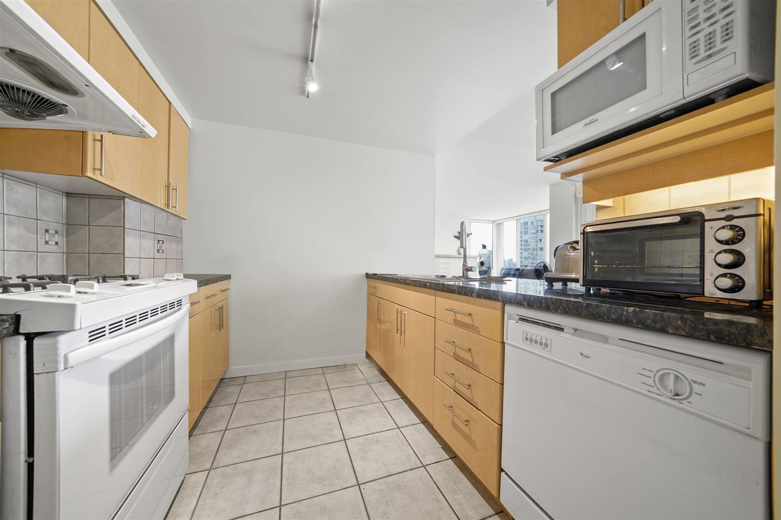 The kitchen from the far end, the gas range and microwave with the dishwasher beside them.