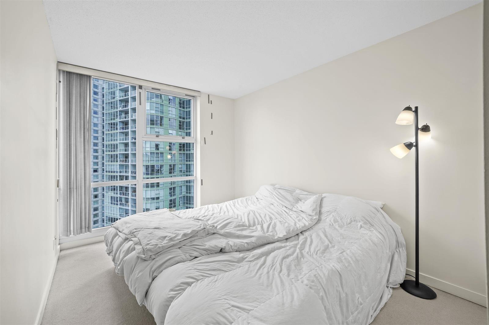 The primary bedroom, a bed under the corner windows with the neighbouring towers filling the glass.