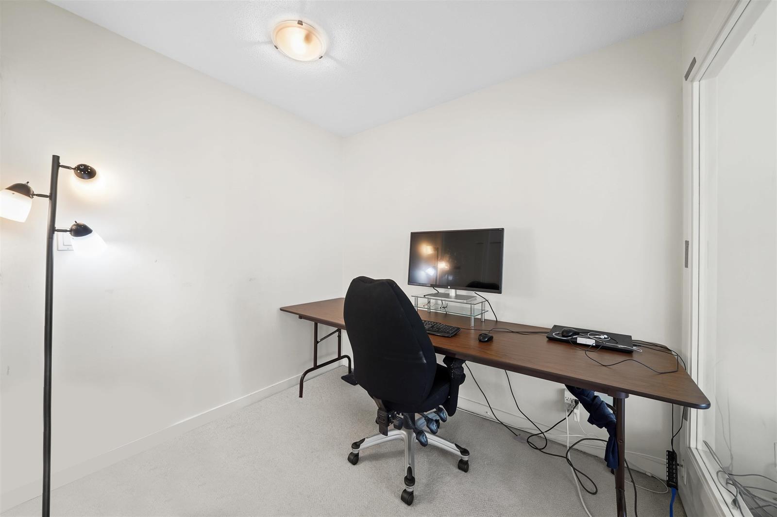 The den from the doorway, the desk along the wall under a floor lamp.