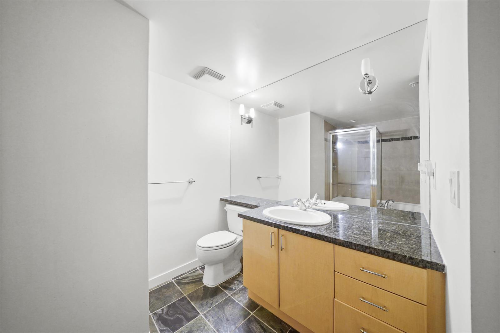 A bathroom, a granite vanity under a full width mirror with the glass shower beside it.