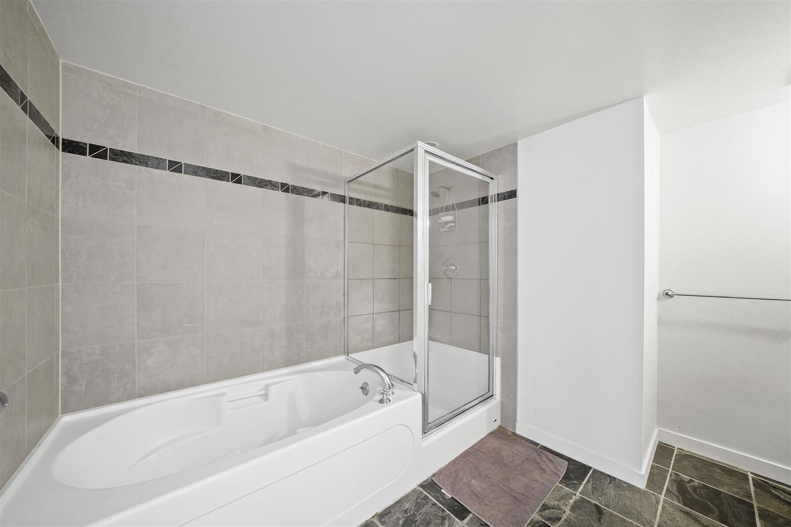 The ensuite, a soaker tub along the tiled wall with a separate glass shower at its end.
