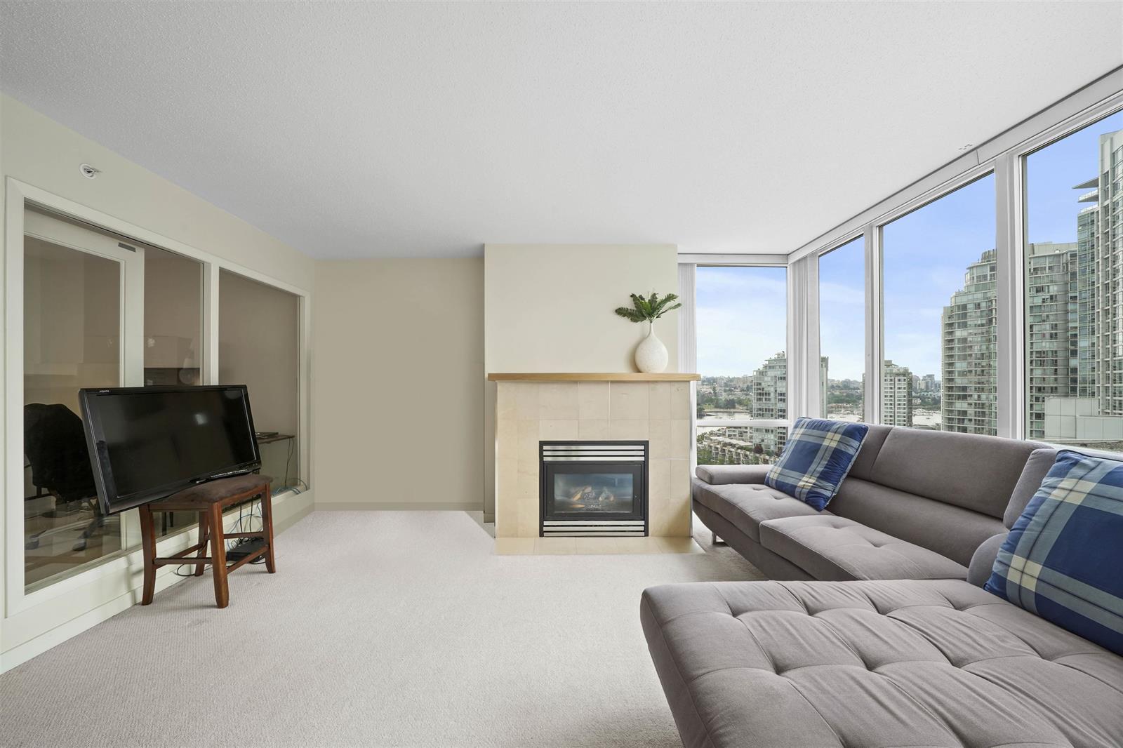 The living room, the gas fireplace on one wall and the windows turning the corner beside it, a sofa drawn up under the glass.