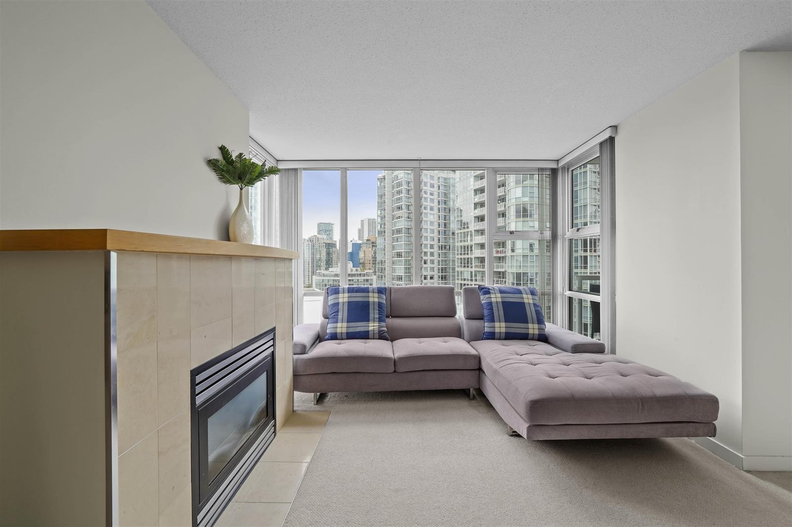 The living room from the fireplace, sofa and chaise under a wall of window with the towers of Yaletown beyond.