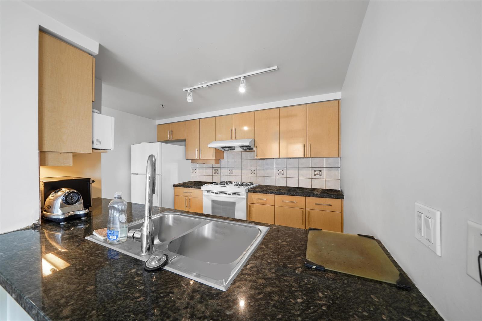 The kitchen from the pass-through, granite counters wrapping to a double sink under maple cabinets.