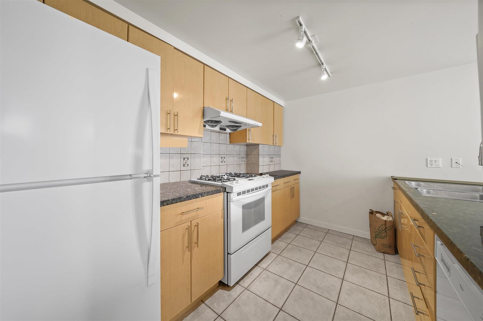 The kitchen along its length, the fridge, the gas range and tile underfoot.
