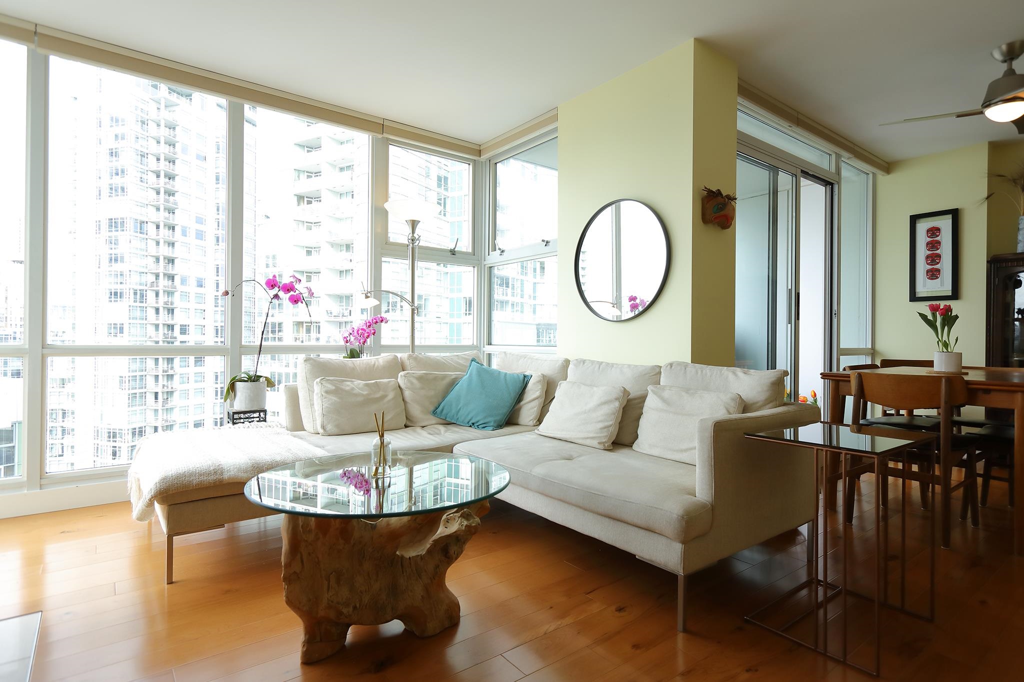 The living room from the corner, a pale sectional under the windows with the dining table beyond it.