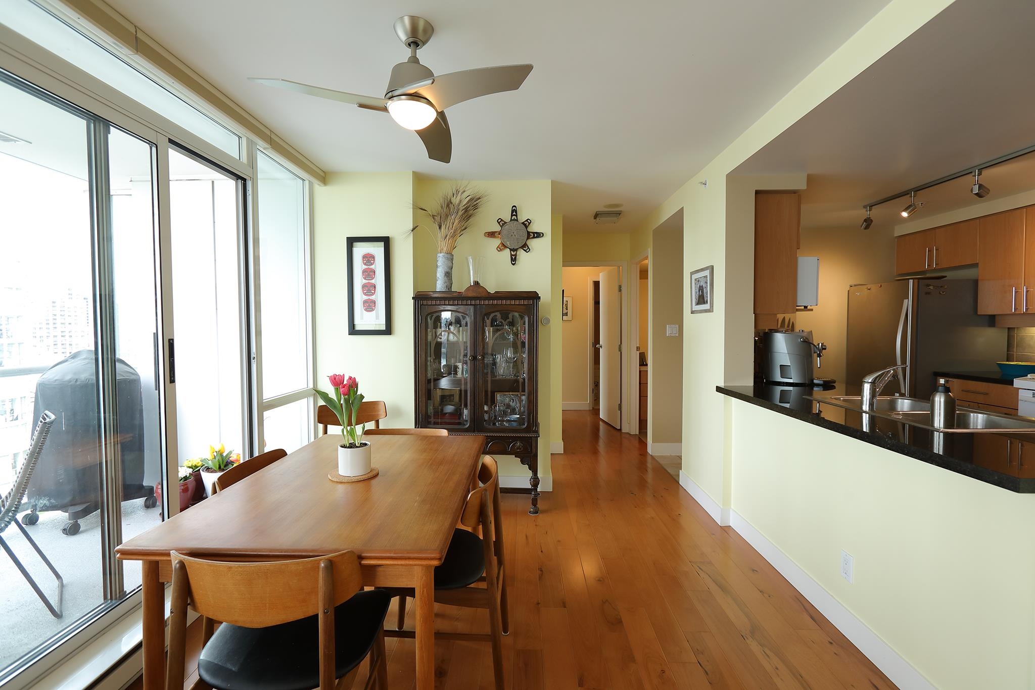 The dining table beside the balcony door, a glazed cabinet behind it and the hall running back past the kitchen counter.