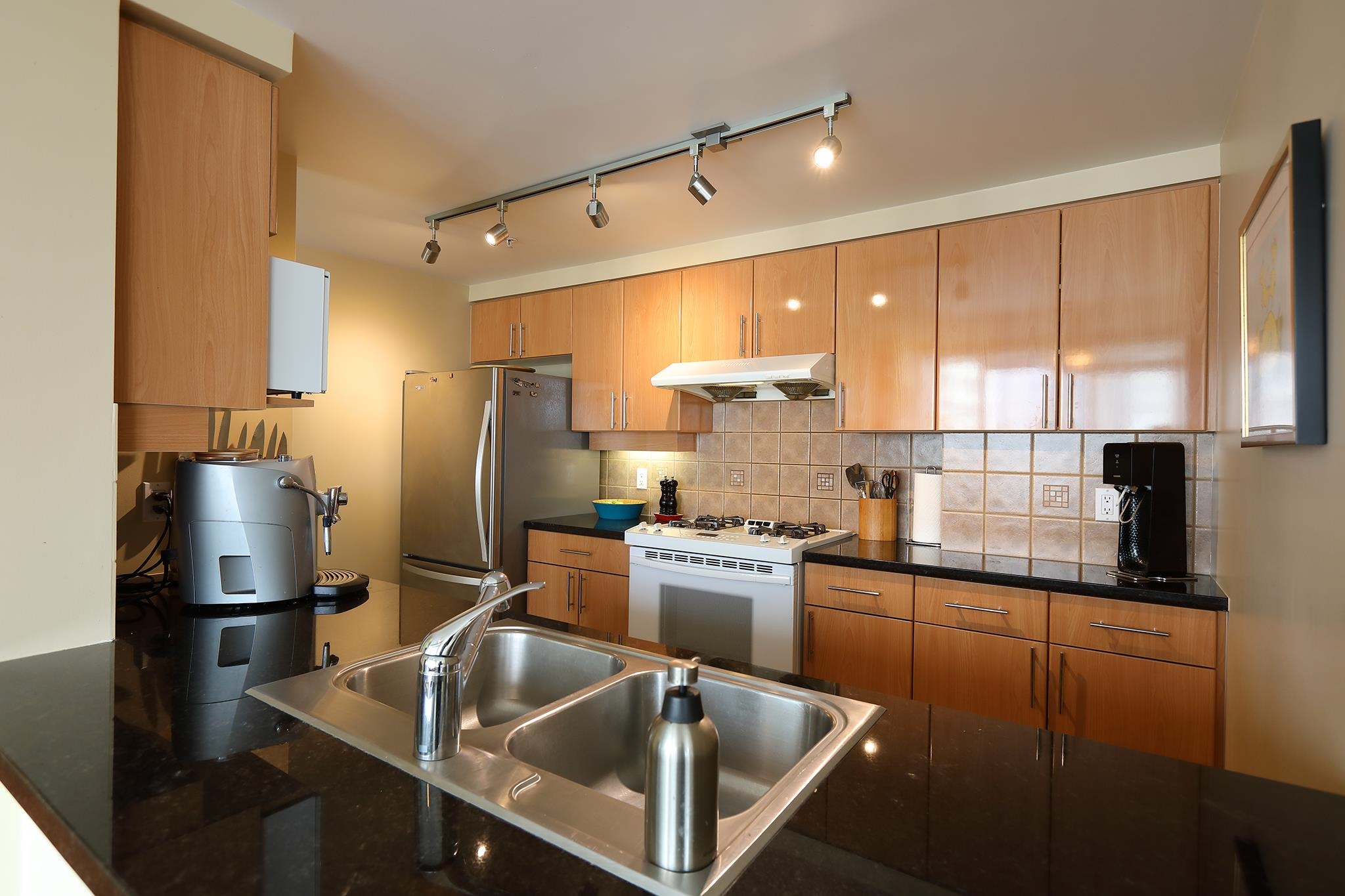 The kitchen behind its granite counter, timber cabinets and a gas range under track lighting.