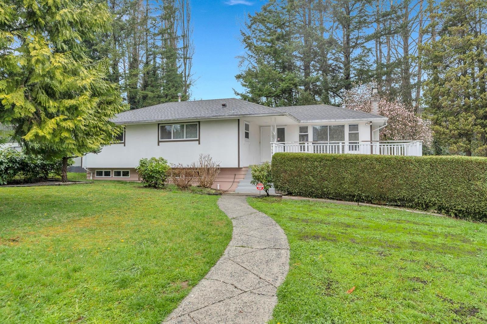 The house from the front lawn, a low two storey behind a clipped hedge with a path curving up to the door.