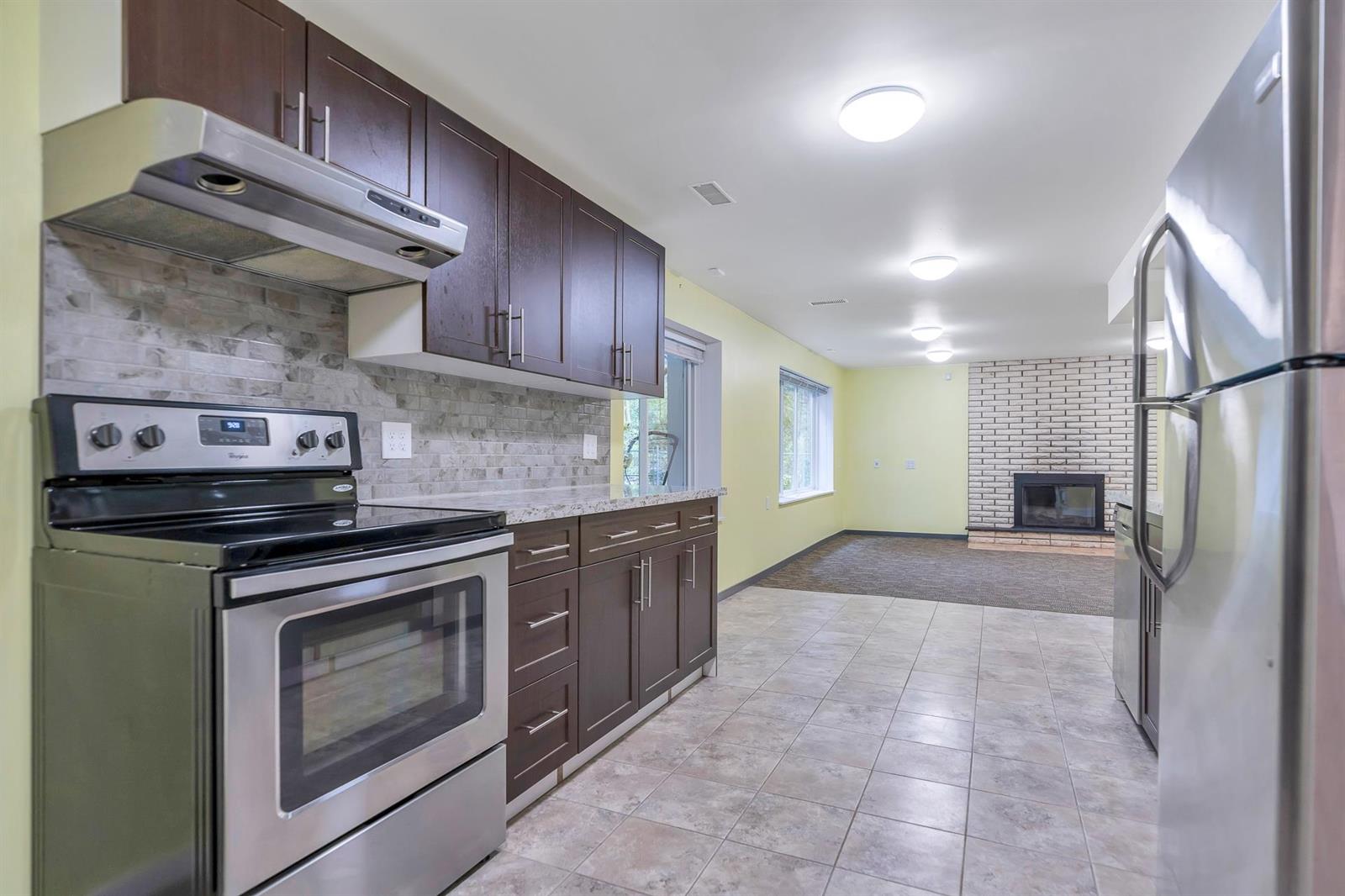 The lower kitchen — a stainless range and refrigerator between dark wood cupboards, with a fireplace at the far end.