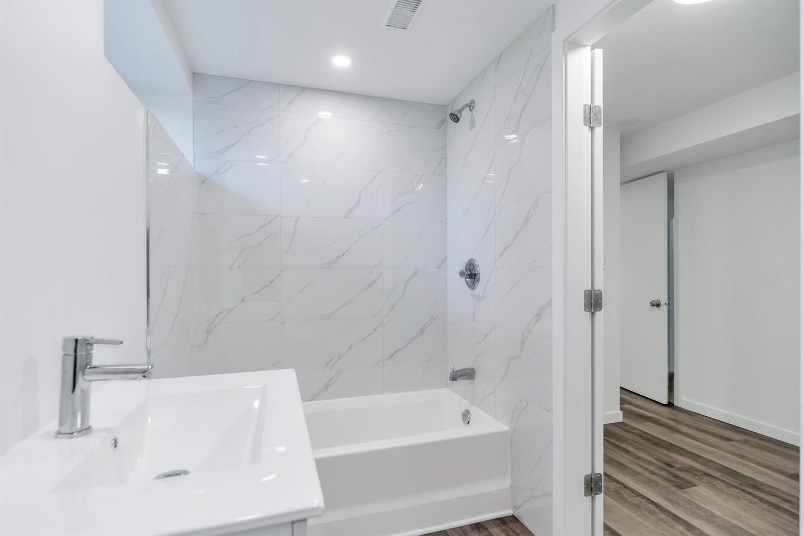 The lower bathroom, a bath and shower lined in marble-patterned tile.