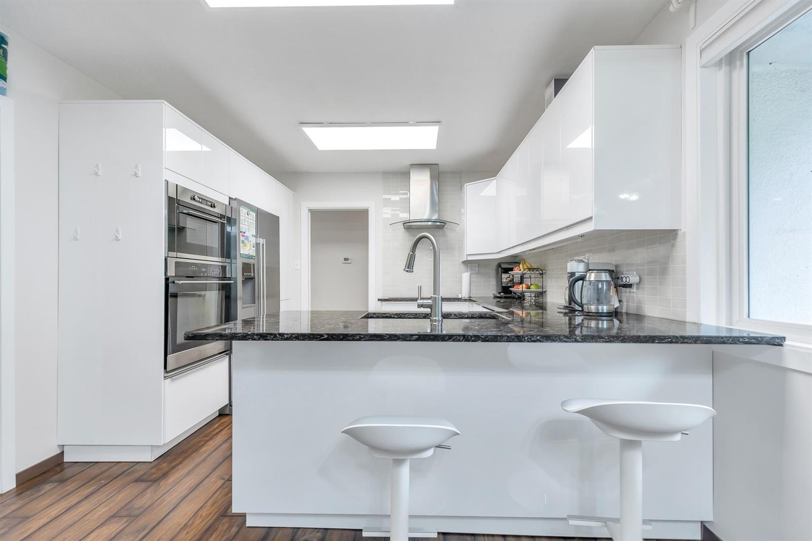 The kitchen: a granite peninsula with two stools, gloss white cupboards, wall ovens and a skylight above.