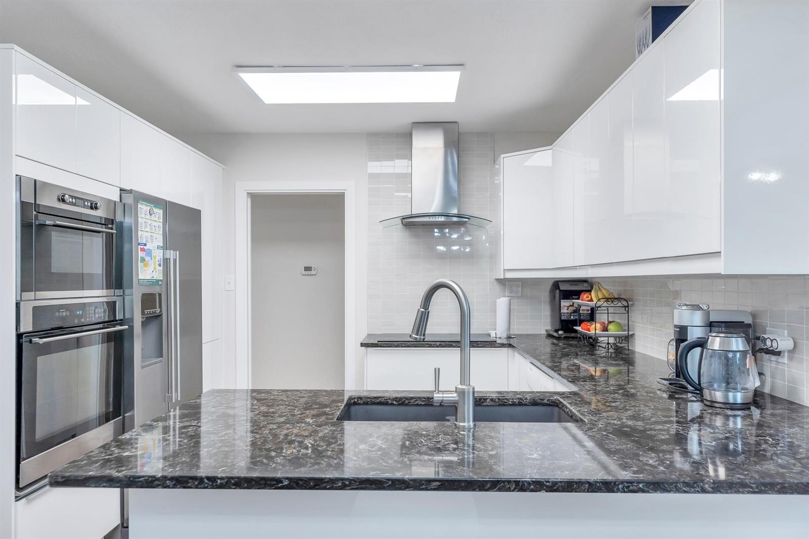 The kitchen counter close in — an undermount sink set in dark granite, with a chimney hood over the cooktop.