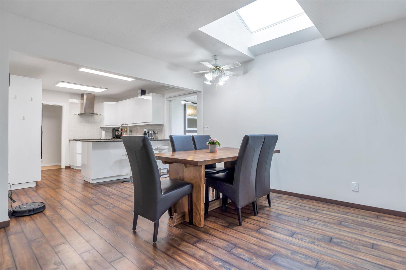 The dining area under a skylight, a timber table and leather chairs between the kitchen and the far wall.