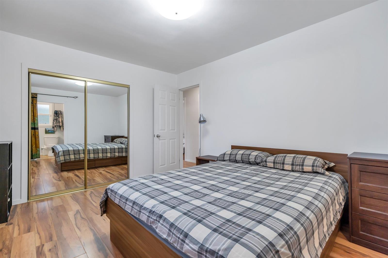 A bedroom with mirrored closet doors along one wall and a chest of drawers opposite.
