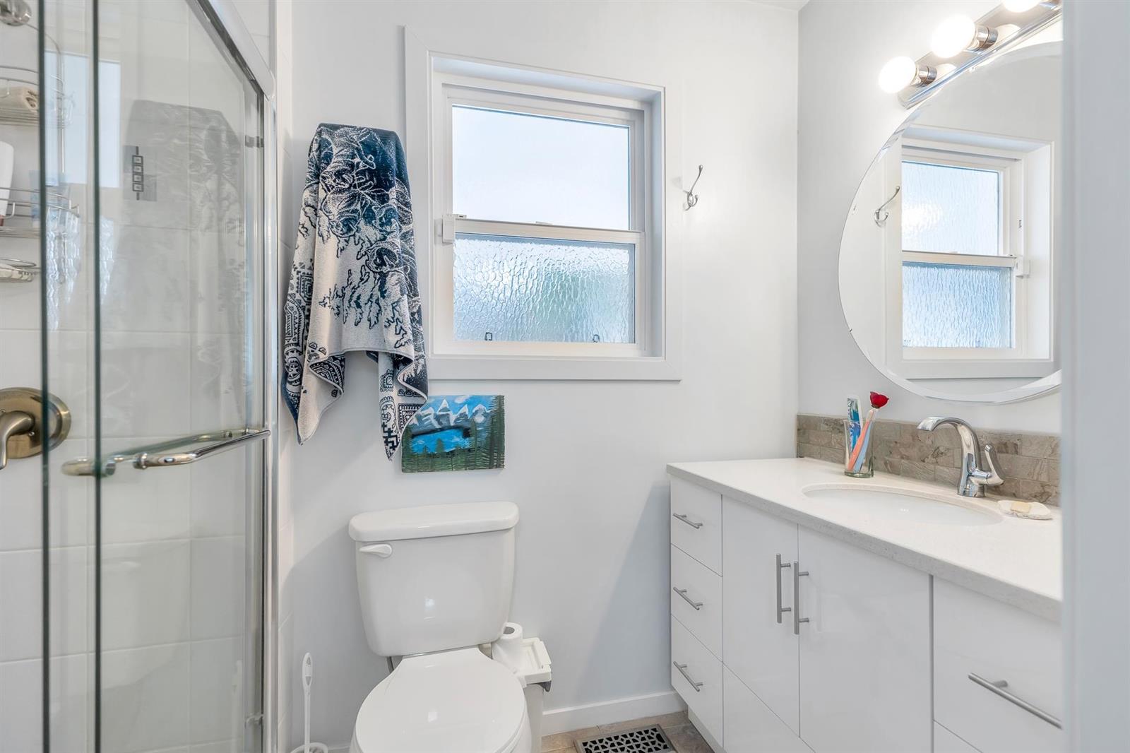 The bathroom, a glazed shower beside the window and a round mirror over the vanity.