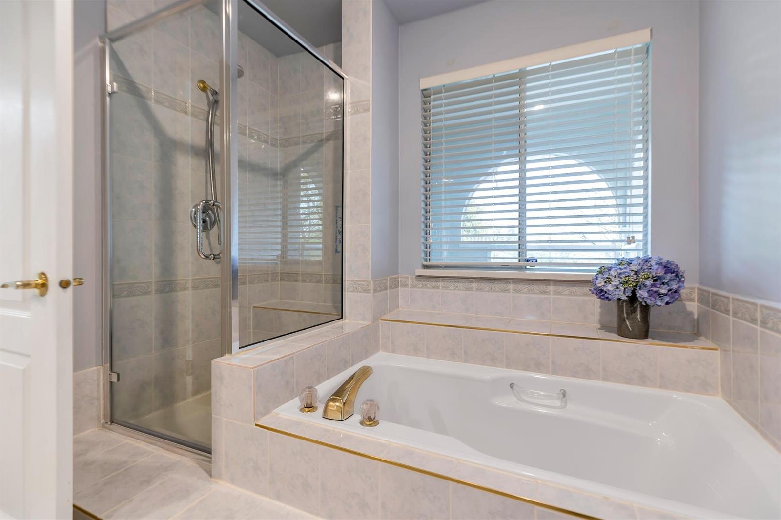 The bathroom, a soaking tub set into tile beside a glazed shower, with a window above it.
