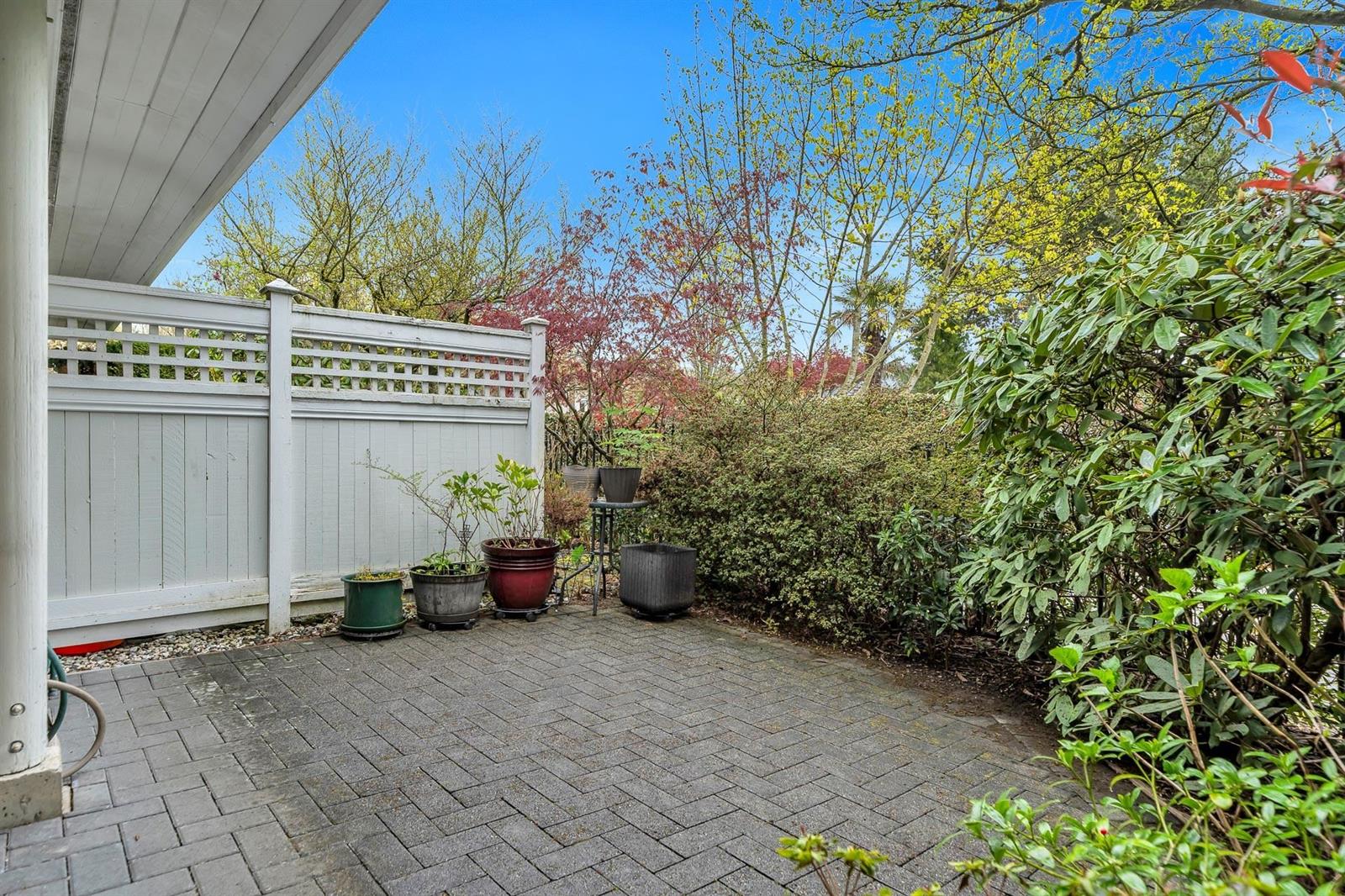 The private patio behind the house, paved and enclosed by a white fence with planting along it.