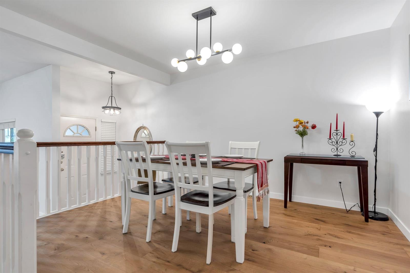 The dining room, a table beneath a bare-bulb chandelier beside the stair rail and the front door.