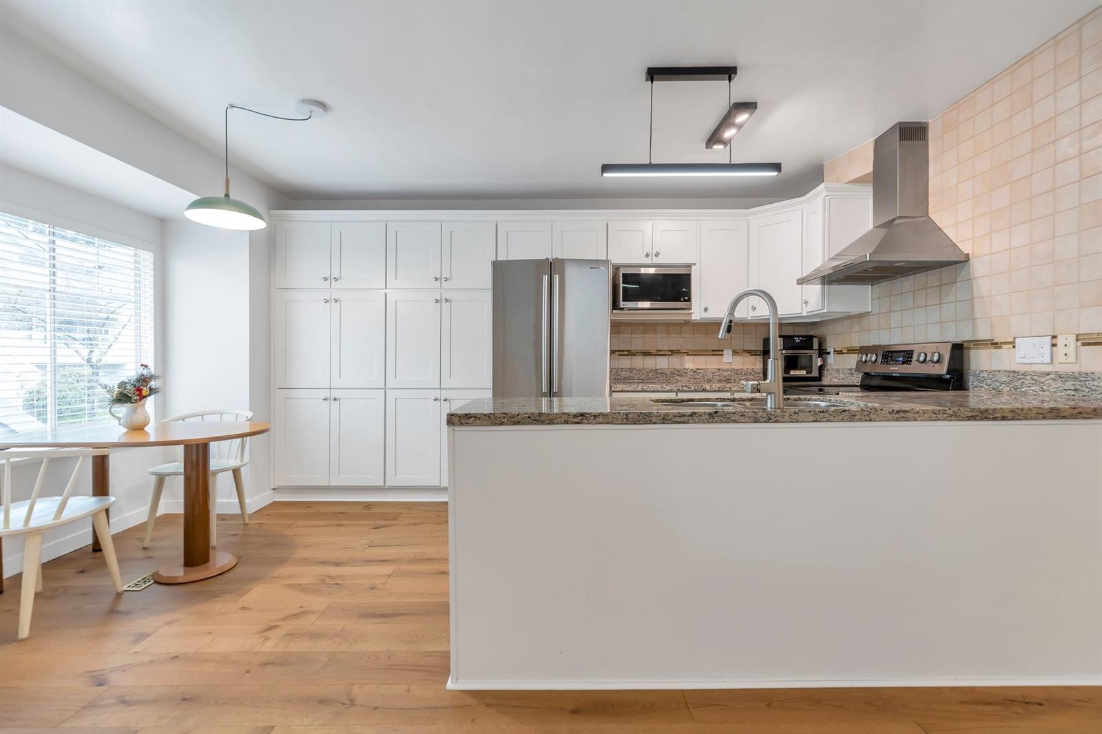 The kitchen: white cupboards and a granite peninsula with a stainless range and refrigerator, the eating nook by the window at the left.