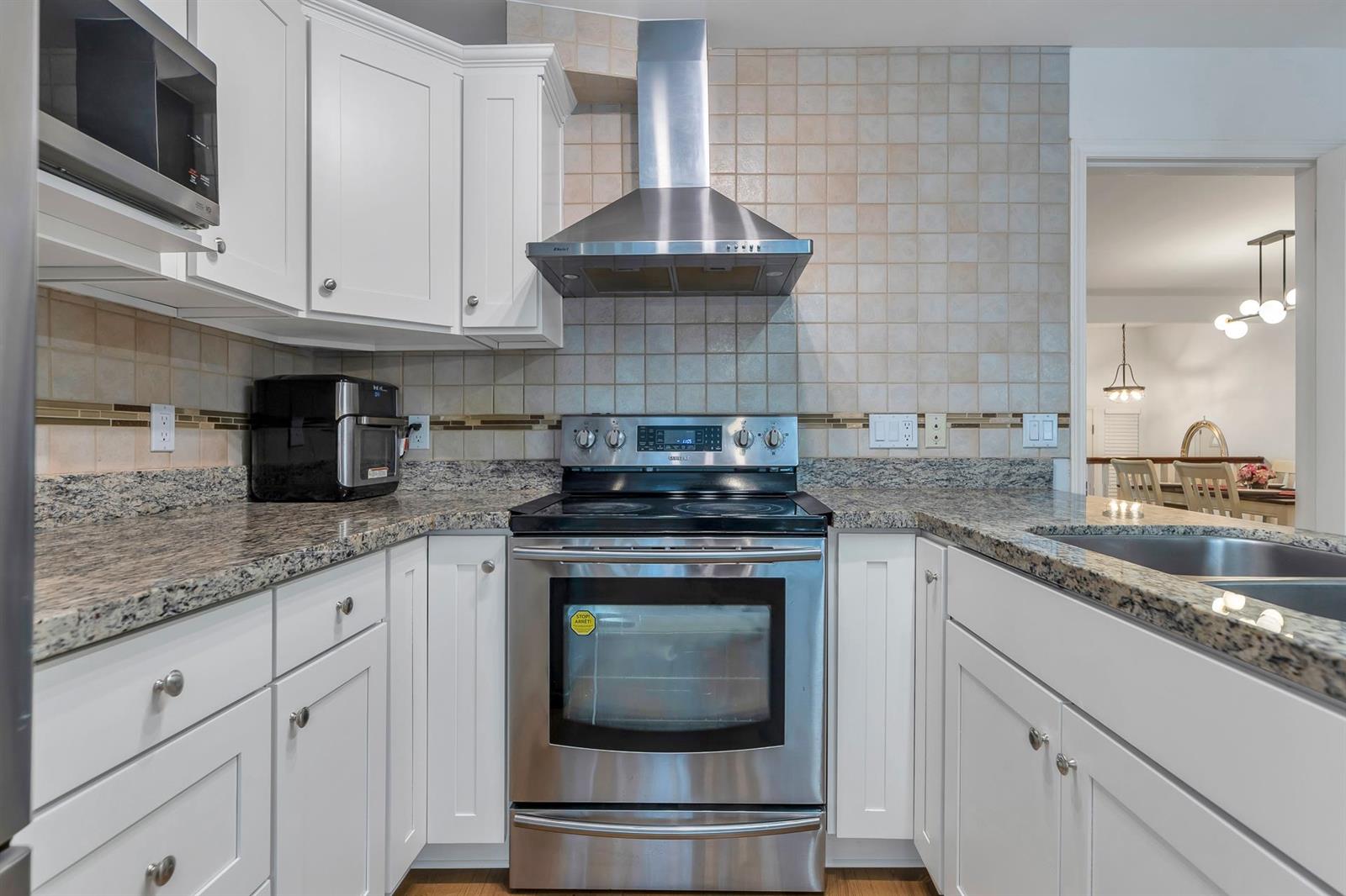 The cooking wall — a stainless range under a chimney hood, tiled splashback and granite counters.