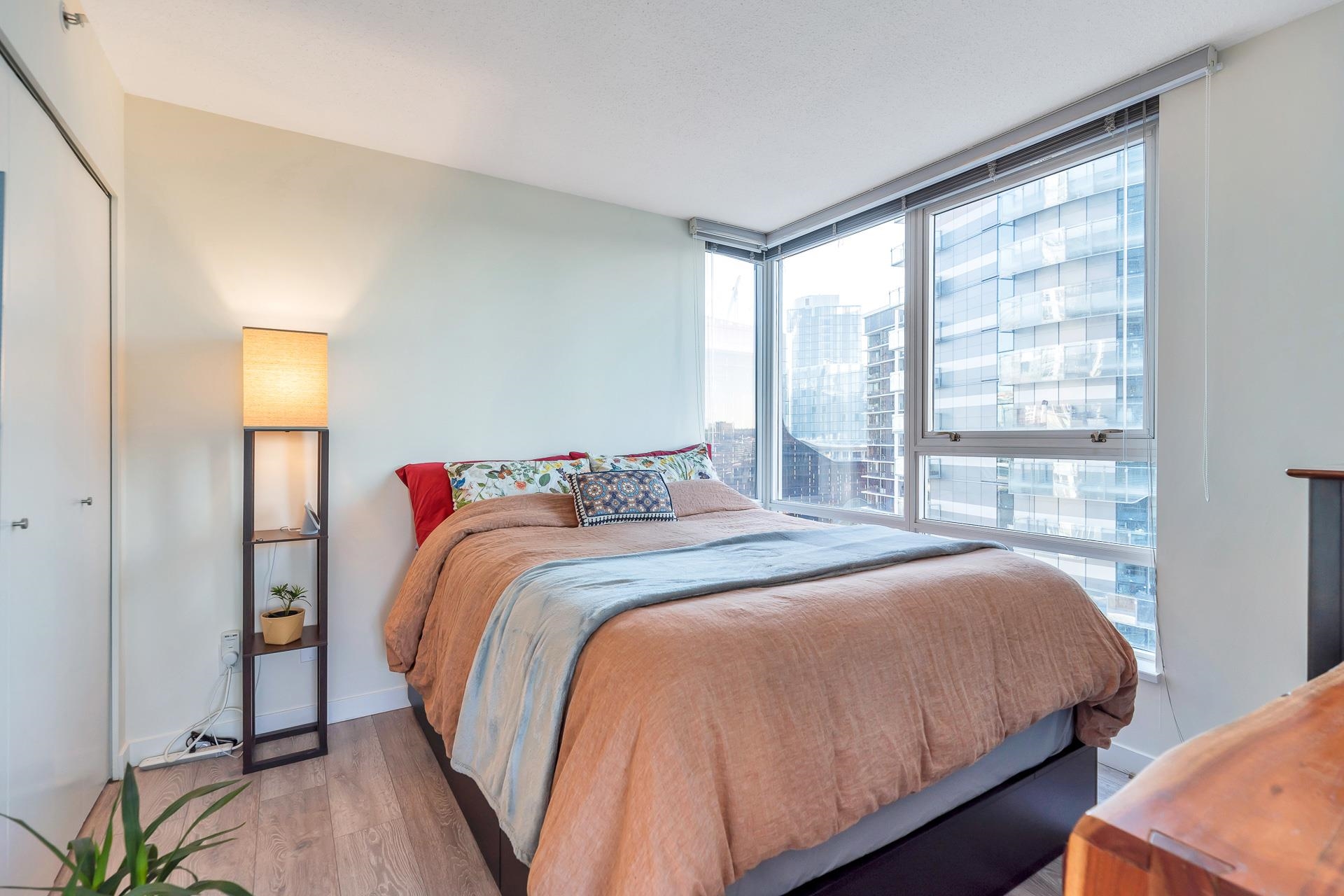 A bedroom, the bed set under windows that wrap the corner.