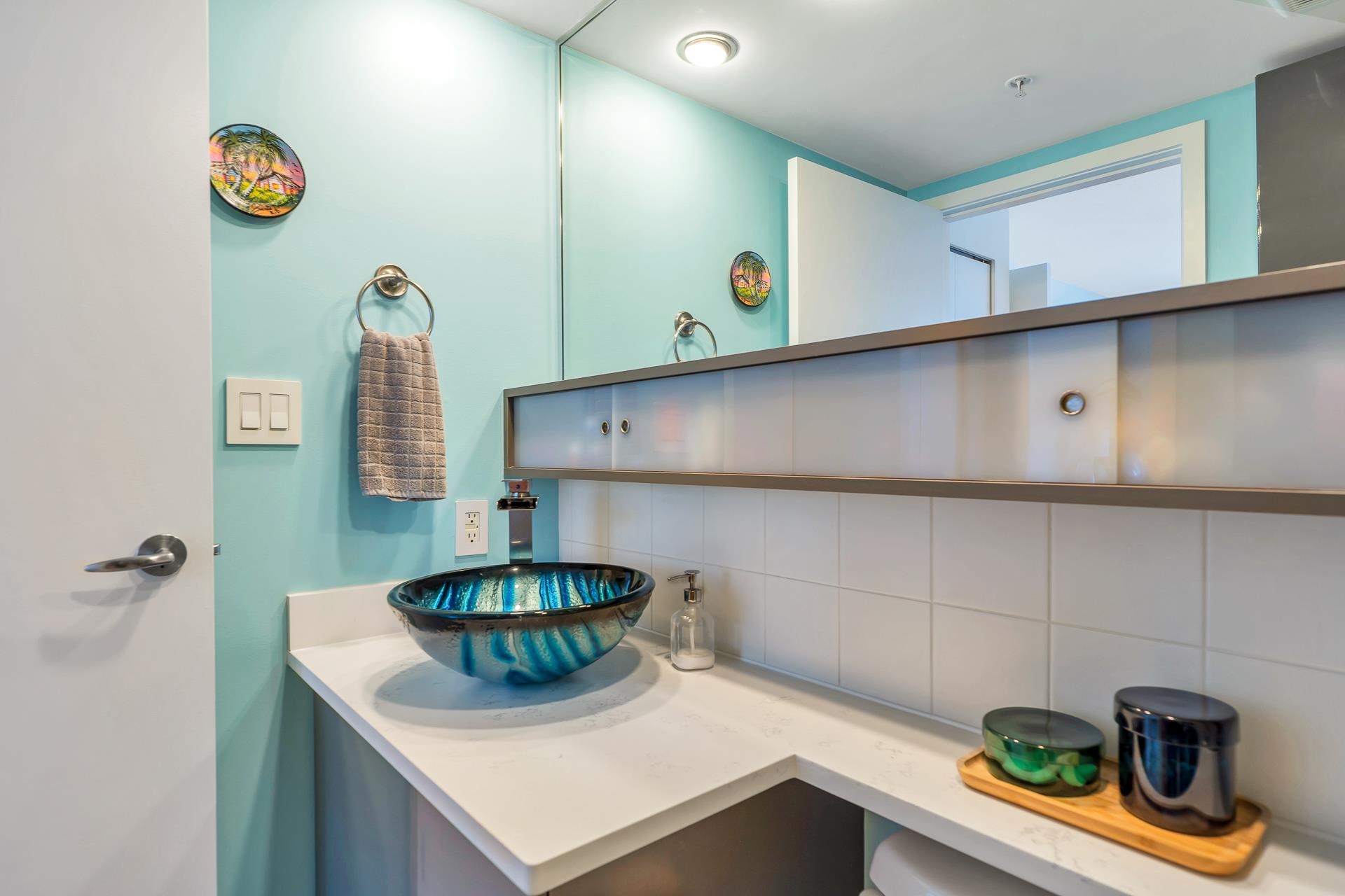 A bathroom, a blue glass bowl set on a quartz counter under a full-width mirror.