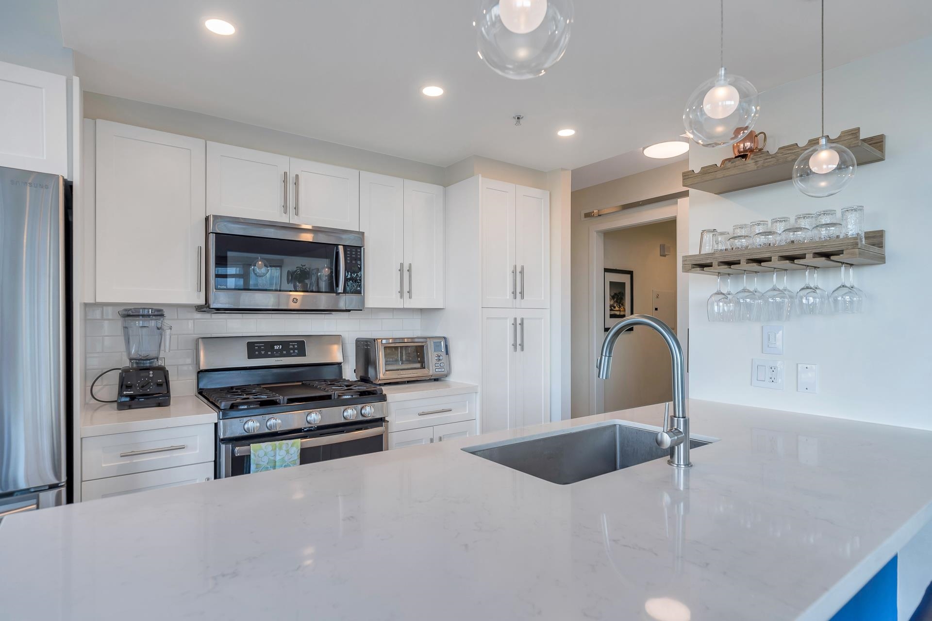 The kitchen, white cabinets either side of a stainless gas range, wine glasses hanging from a timber rack.