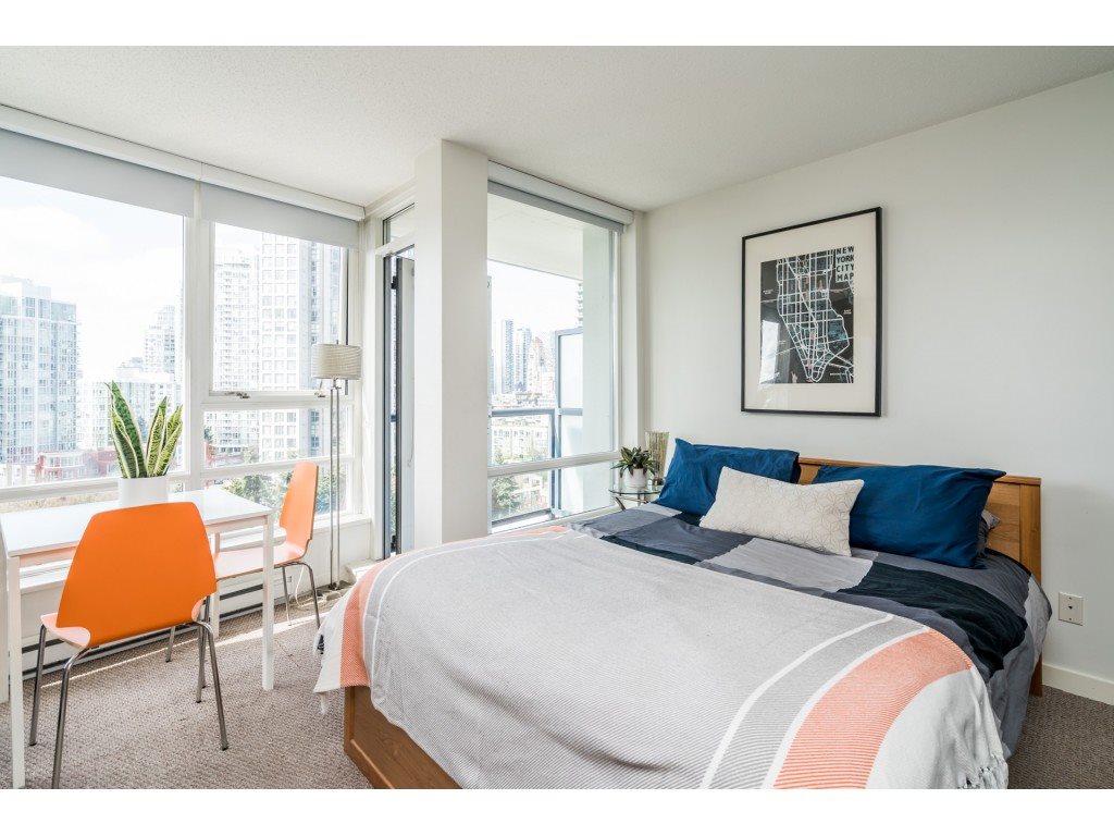 The bed under the windows, a print above the headboard and an orange chair at the table beside it.