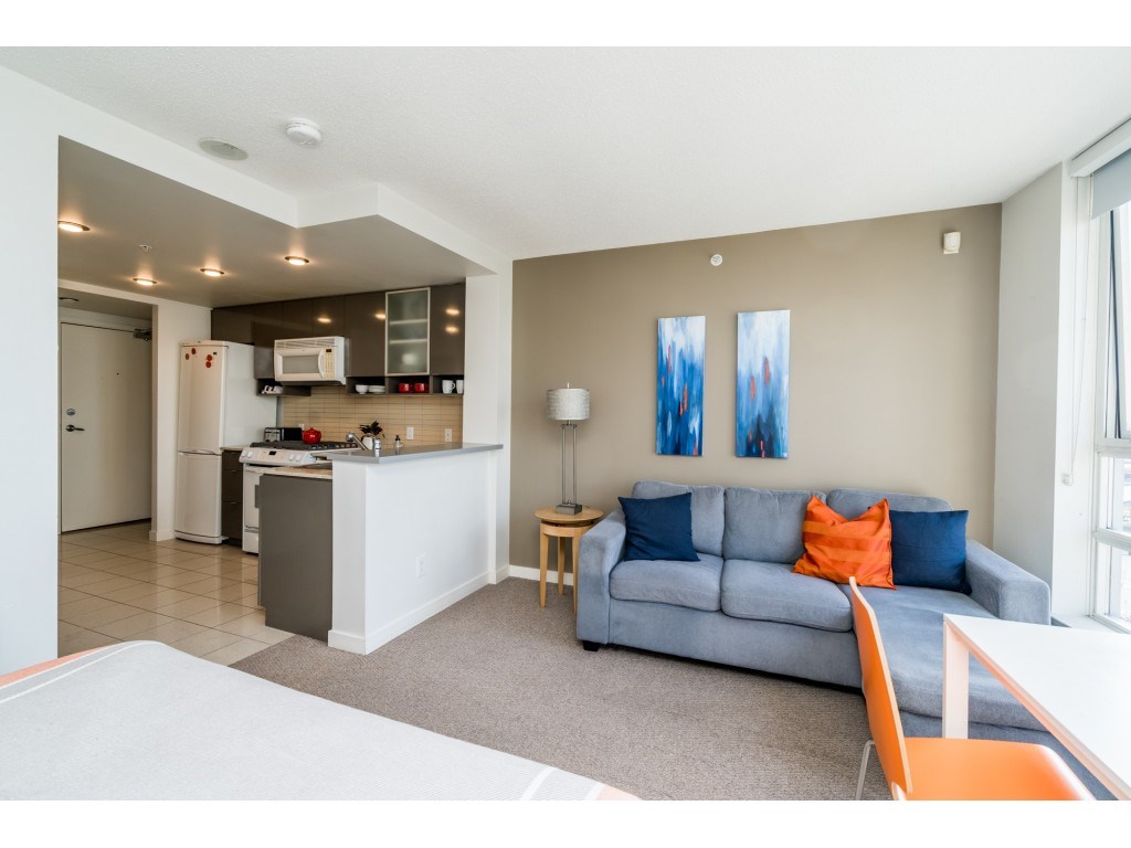 The living area toward the kitchen, a grey sofa with orange cushions and two prints on the wall.