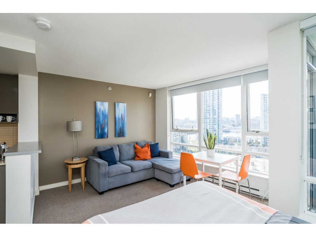 The sofa and the table by the windows, the room seen from the sleeping end.