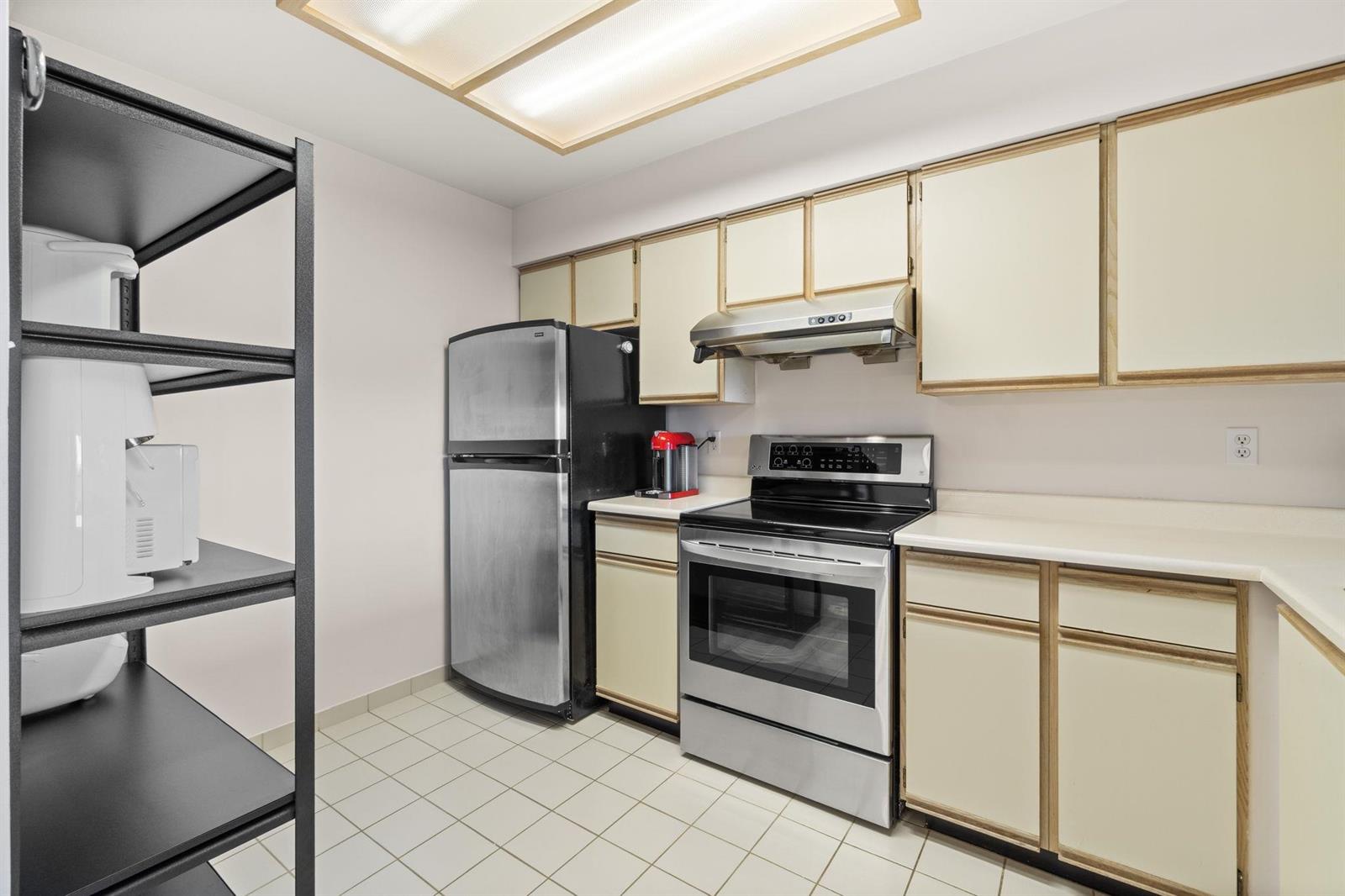 The kitchen from the far corner, the refrigerator beside a run of shelving.