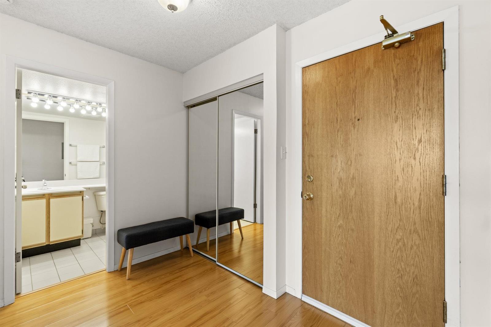 The entry, a bench in front of mirrored closet doors with the front door on the right.