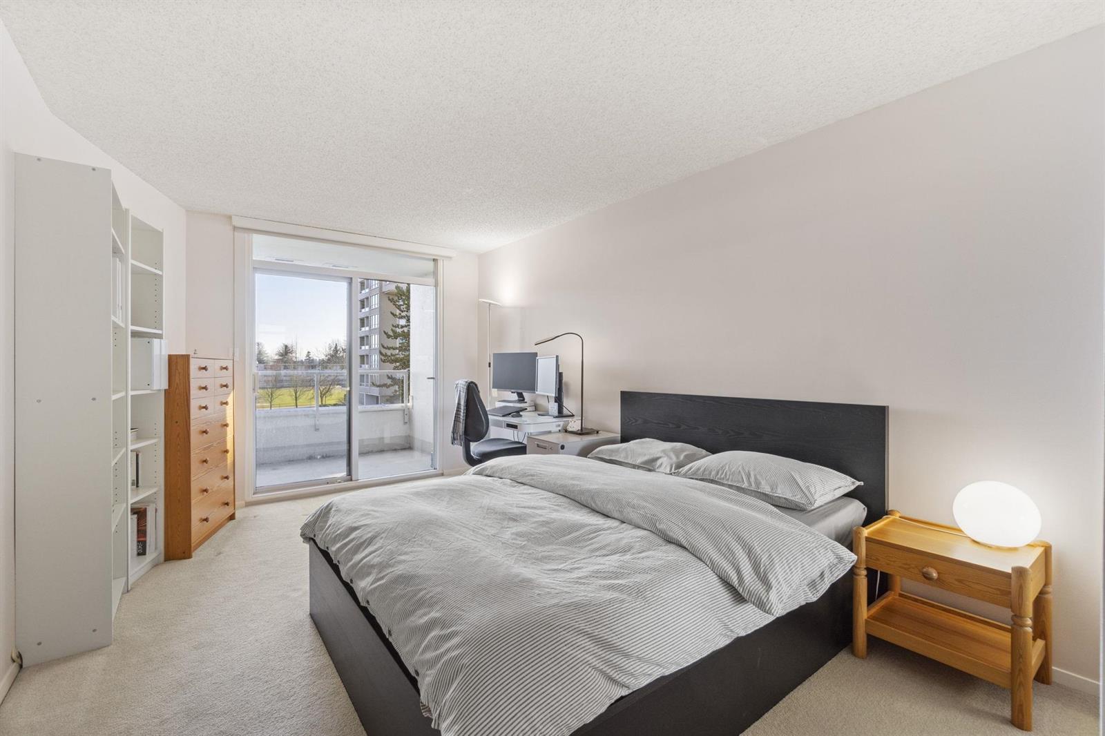 The bedroom, a bed against the wall with the balcony door and windows on the left.