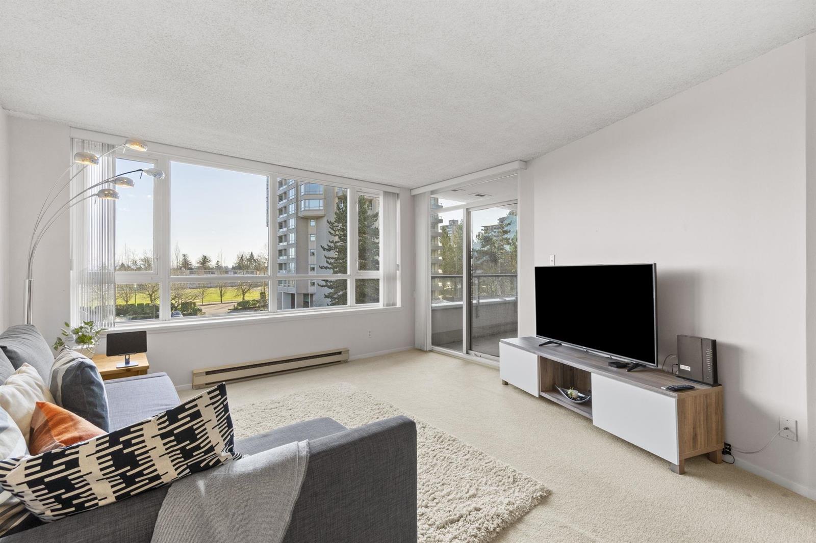 The living room from the dining end, the television along one wall and the balcony door beyond the seating.